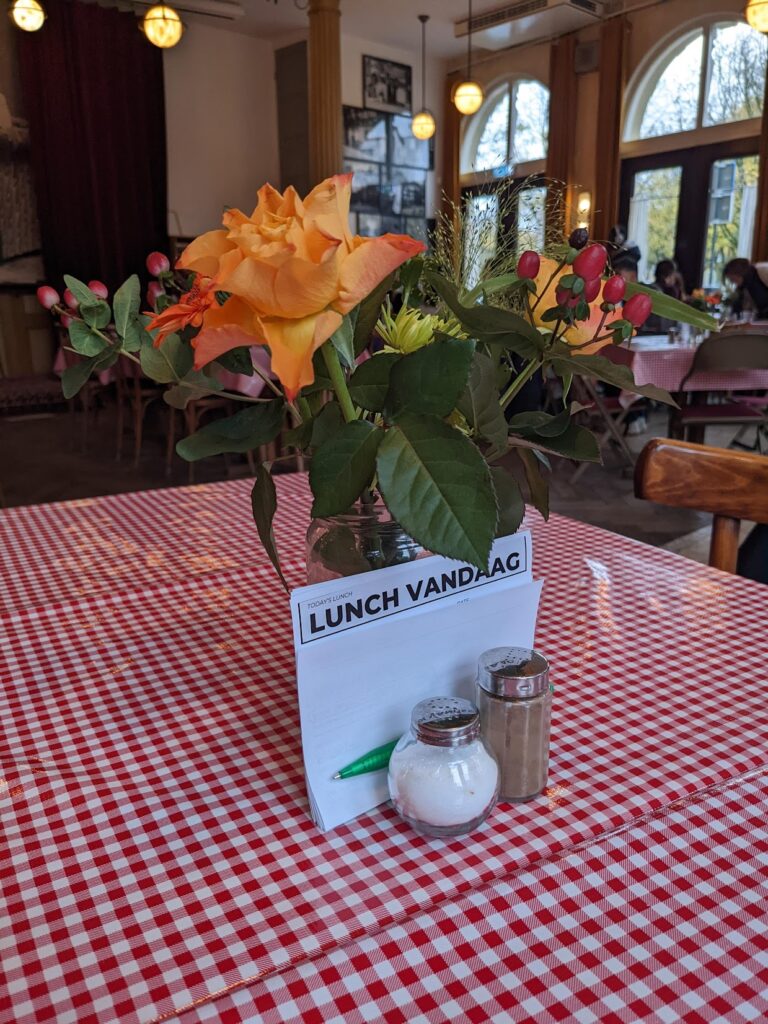 Red plaid dining table featuring a paper survey titled "Lunch Vandaag" between a bouquet center piece and salt and pepper